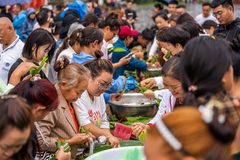 6月7日，游客在貴州省畢節市黔西新仁苗族鄉化屋村體驗包粽子。