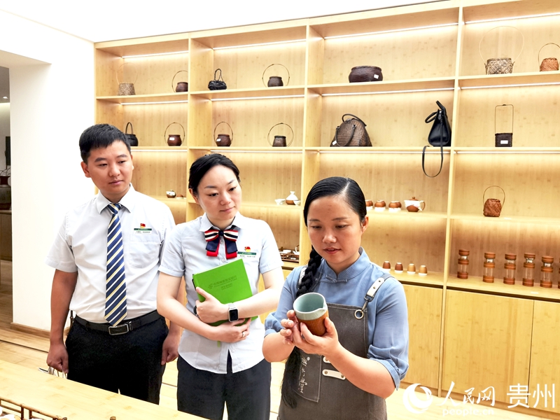 楊昌芹（左）給郵儲銀行赤水市支行工作人員展示“竹包瓷”茶具。人民網記者 王秀芳攝